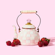 MacKenzie Childs | Rosy Check Tea Kettle, 2 QT: Ceramic teapot in a pink-and-white checkerboard pattern with brass accents, wooden handle, and surrounded by fresh strawberries.