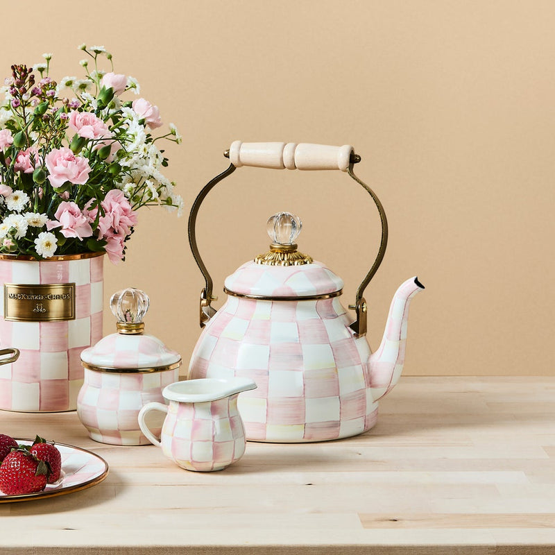 MacKenzie Childs | Rosy Check Tea Kettle, 2 QT, with pink-and-white checkerboard design, brass handle, and glass finial, elegantly displayed with matching accessories and flowers.