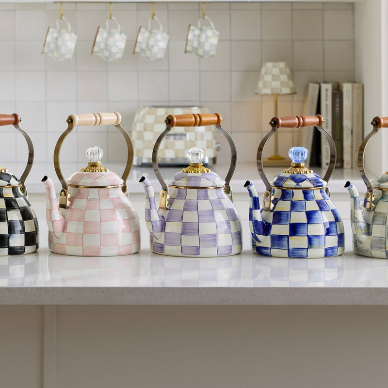 MacKenzie-Childs Violet Check Tea Kettle, 2 Qt, sits elegantly on a white countertop, surrounded by matching checkered kitchenware, showcasing its distinctive hand-painted design.