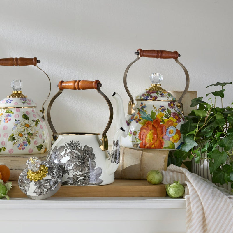 MacKenzie-Childs White Flower Market 2 Quart Tea Kettle with floral patterns, wood handle, and glass-topped lid, displayed on a wooden ledge with tomatillos and trailing ivy.