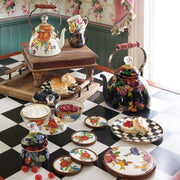 MacKenzie Childs | White Flower Market 2 Quart Tea Kettle on a checkerboard table with floral teapots, scones, and matching floral-patterned china, embodying vintage English-tea style.