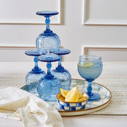 MacKenzie-Childs Sterling Check Round Tray with cobalt-blue goblets, lemon wedges, and a striped linen napkin, creating a vibrant, summery tabletop display.