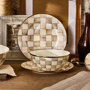 Mocha Check Small Everyday Bowl by MacKenzie Childs, hand-painted with coffee checks, sits on a plate with rustic decor, embodying warm, rustic-chic style.