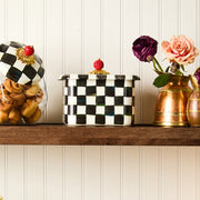 MacKenzie-Childs Courtly Check Recipe Box on a wooden shelf, surrounded by a glass canister of pastries and copper vases with flowers, showcasing elegant kitchen storage.