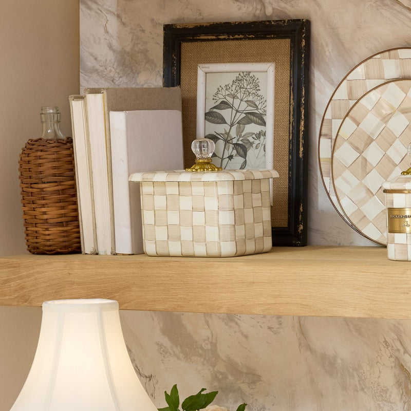 MacKenzie-Childs Mocha Check Recipe Box on a wooden shelf with glass knob, surrounded by home décor: wicker bottle, books, botanical print, and woven container.