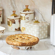 MacKenzie-Childs Mocha Check Recipe Box on a marble countertop, featuring a hand-painted design, glass knob, and brass accents, alongside a floral pie dish and decorative canisters.