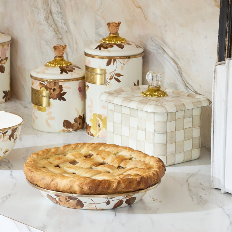 MacKenzie-Childs Mocha Check Recipe Box on a marble countertop, featuring a hand-painted design, glass knob, and brass accents, alongside a floral pie dish and decorative canisters.