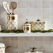 MacKenzie-Childs Mocha Check Recipe Box with glass knob and brass accents, displayed with matching utensils and decorative evergreens on a kitchen shelf.