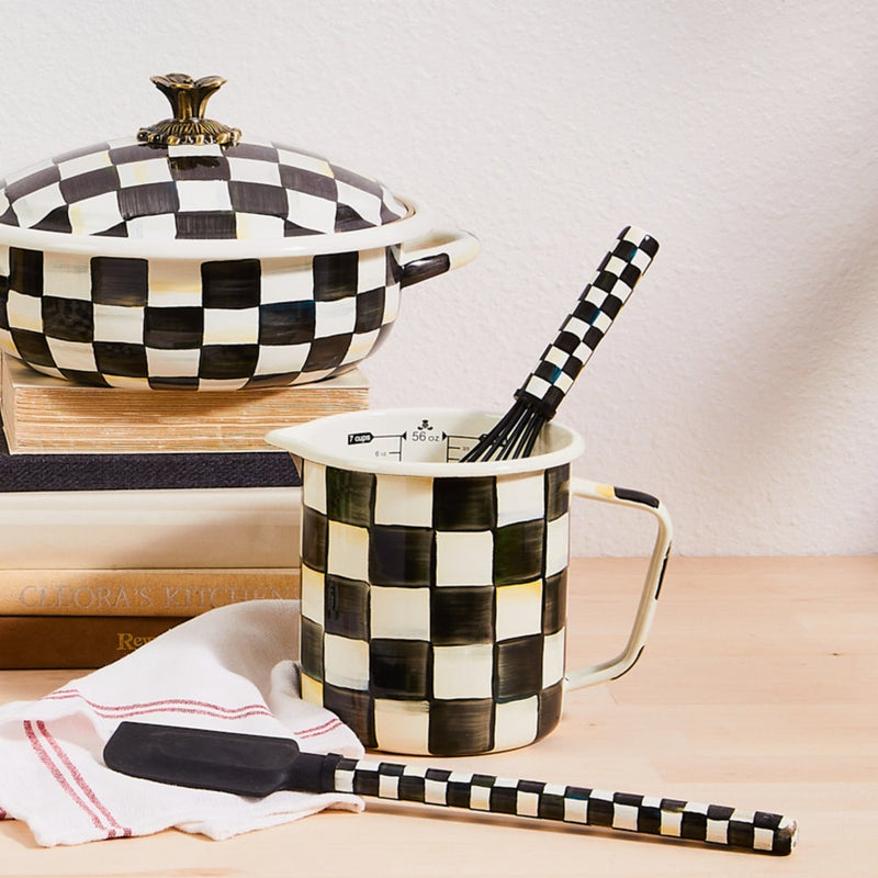 MacKenzie-Childs | Courtly Check 7 Cup Measuring Cup on a kitchen tabletop, featuring a hand-painted checkerboard design with a whisk inside.