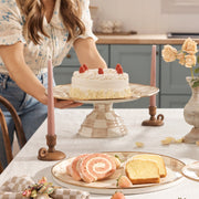 MacKenzie Childs | Mocha Check Large Pedestal Platter elegantly displays a white-iced cake, surrounded by sliced cakes and strawberries, set on a beautifully arranged tabletop.