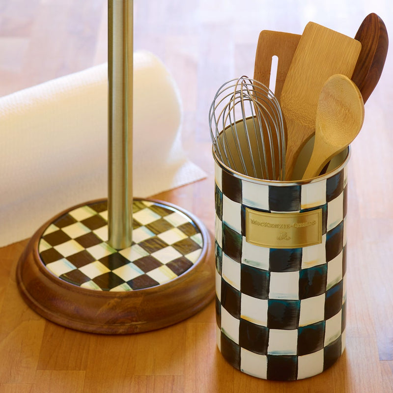 MacKenzie Childs | Courtly Check Utensil Holder on a countertop, holding a whisk and wooden utensils. A matching paper towel stand sits nearby, both featuring a checkerboard pattern.