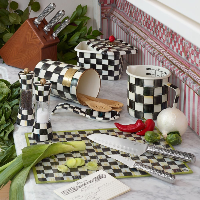 MacKenzie Childs | Courtly Check Utensil Holder with wooden spoons, surrounded by checkered kitchen items, knives, and fresh produce on a marble countertop.