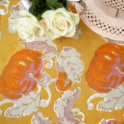 Close-up of Caravan Home - Pumpkin Orange & Mustard Tablecloth, featuring stylized pumpkins, with a silver creamer of white roses and a straw hat accenting the fall theme.