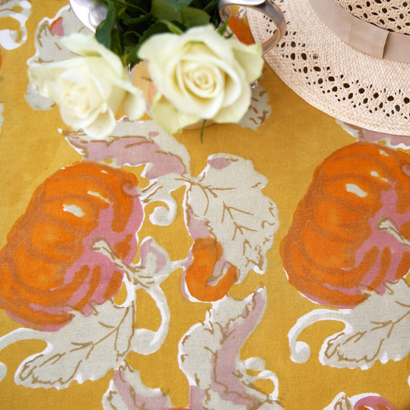 Close-up of Caravan Home - Pumpkin Orange & Mustard Tablecloth, featuring stylized pumpkins, with a silver creamer of white roses and a straw hat accenting the fall theme.