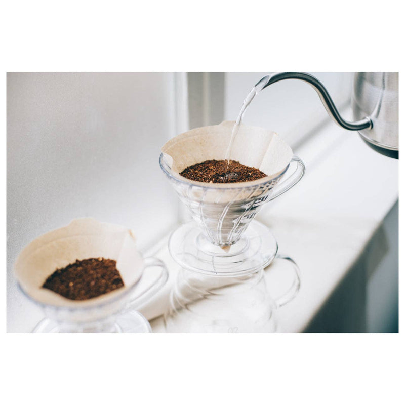 V60 pour-over setup with HARIO USA - V60 Paper Filters: White/100 Sheets Boxed, showcasing seamless water flow into a glass server for refined coffee brewing.