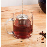 HIC Kitchen Barrel Tea Infuser, Large, in double-walled glass mug with dark tea, loose tea leaves, and dried fruit bits on wooden surface.