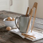 bambu® - Small Bamboo Tongs on a rustic kitchen table, displayed with brown eggs and a ceramic pitcher, capturing a warm, natural kitchen aesthetic.
