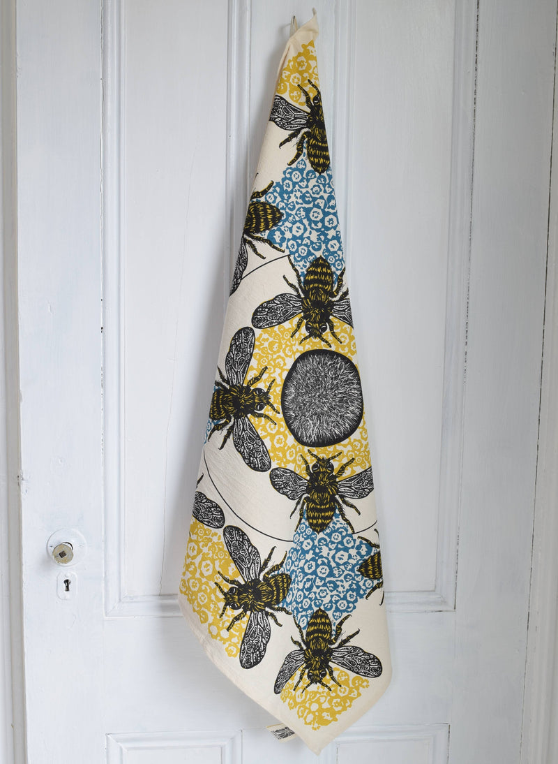 Hearth and Harrow - Honeybee Tea Towel - Organic Cotton - Oversized 30x30, featuring detailed bee motifs on honeycomb, hangs from a wooden door, showcasing its vintage-inspired design.