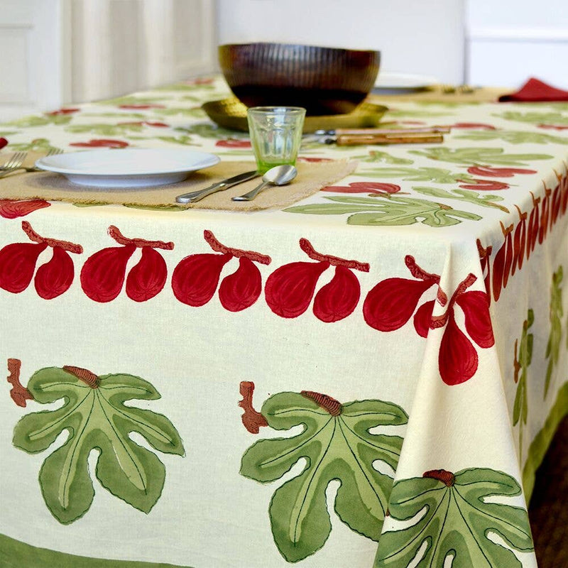 Couleur Nature - Fig Red & Green tablecloth with fig motifs adorns a dining table set with a plate, tumbler, utensils, and wooden bowls.