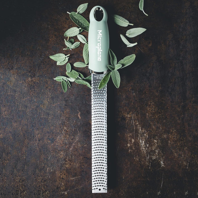 Microplane | Premium Zester, Grater - Sage Green with stainless-steel blade, surrounded by fresh sage leaves on a dark surface, ideal for versatile grating tasks.