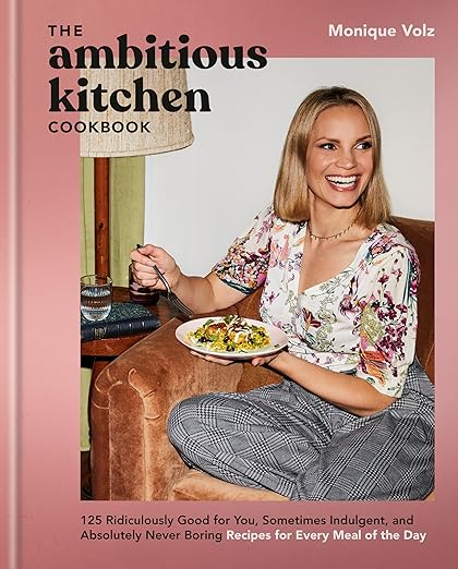 The Ambitious Kitchen Cookbook by Monique Volz, featuring 125 creative, nutritious recipes, with the author holding a plate of food, embodying vibrant, healthy cooking.