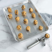 Nordic Ware Small Cookie Dropper, displayed on a baking sheet, ensures uniform 2–3 inch cookies with its ergonomic, 1.5-tablespoon stainless steel scoop for easy baking.