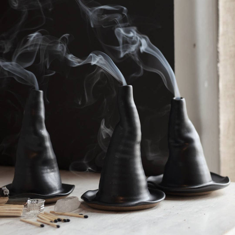 Gravesco Pottery - Witch Hat Incense Burner: Three black, ceramic witch hat incense holders emit smoke, surrounded by matches and ritual accessories on a light surface.