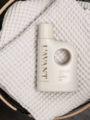 L’AVANT Collective - Laundry Detergent Fresh Linen, off-white bottle with built-in handle, sits on white cloth, highlighting its eco-friendly, concentrated formula for effective, gentle cleaning.