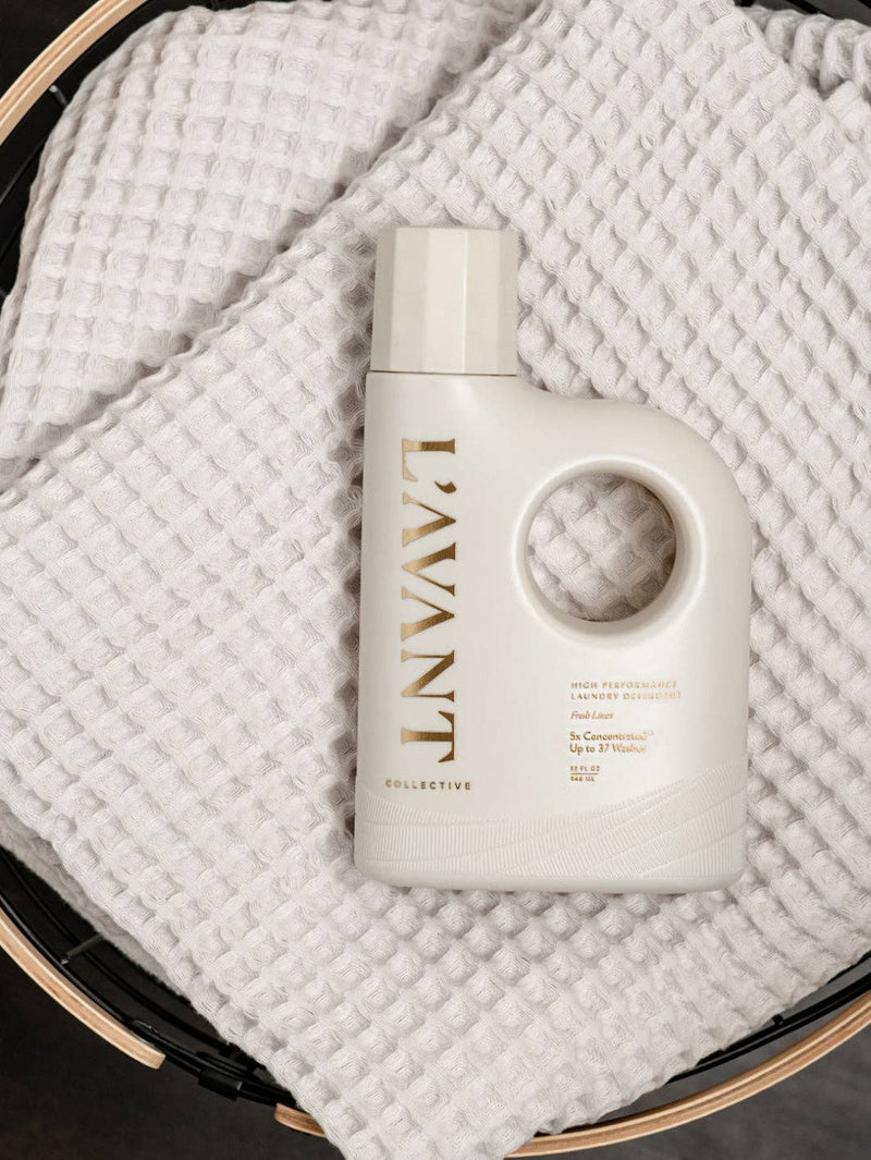 L’AVANT Collective - Laundry Detergent Fresh Linen, off-white bottle with built-in handle, sits on white cloth, highlighting its eco-friendly, concentrated formula for effective, gentle cleaning.