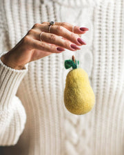 Hand holding Farmhouse Pottery - Felted Fruit Ornament: Pear, a small wool ornament with a green leaf and brown stem, handcrafted in Nepal.