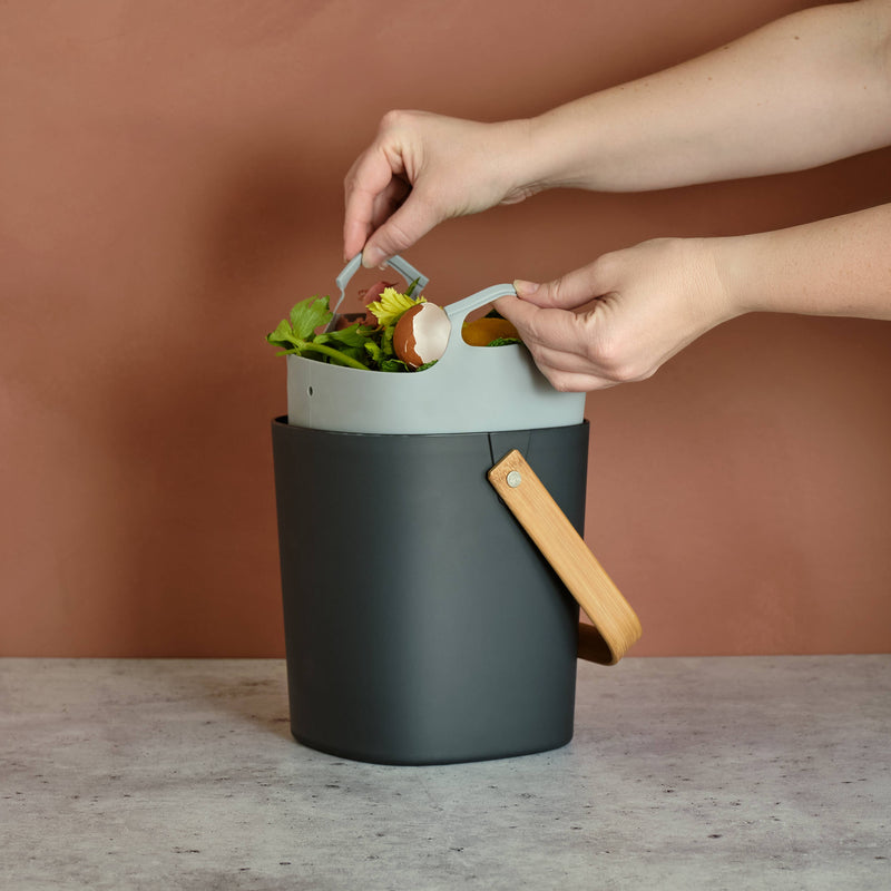 Hands using Bamboozle - Composter Reusable Liner to dispose of plant waste in a trash can, showcasing its practical design and functionality.