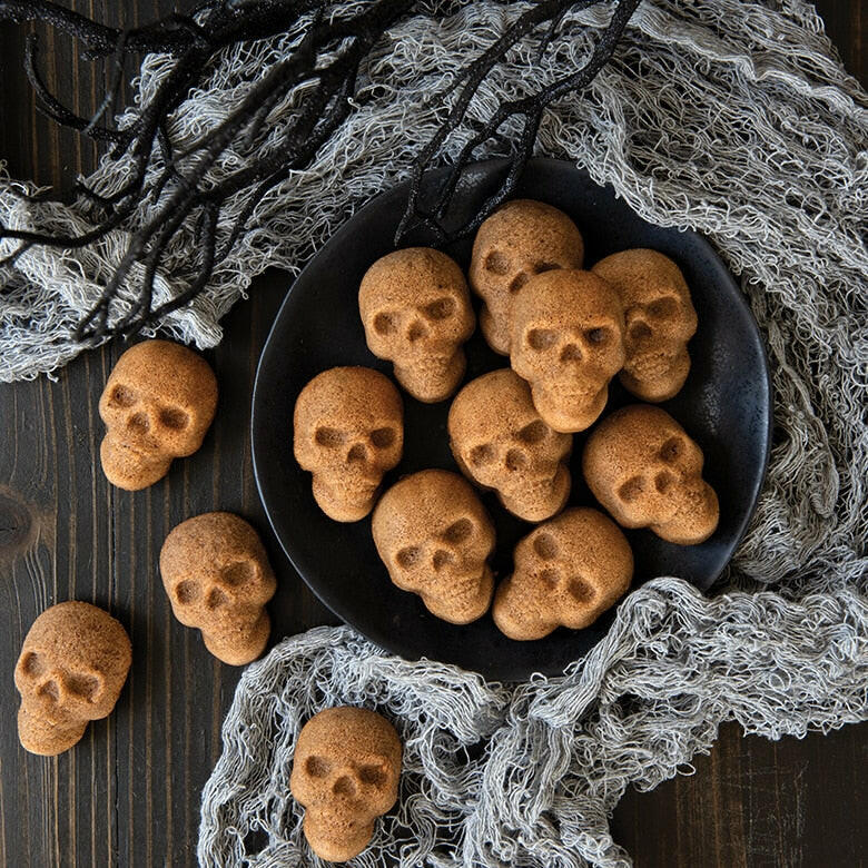 Nordic Ware | Skull Cakelet Pans - Skull Bites: A spooky display of skull-shaped mini cakes on a black plate, perfect for Halloween-themed baking.