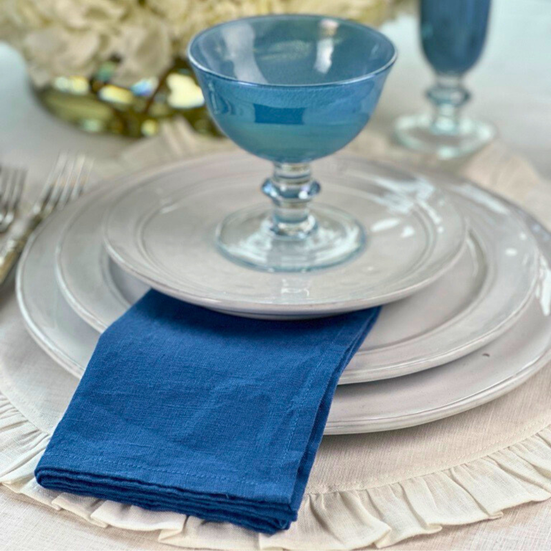 Crown Linen Designs' Washed Linen Napkin Sets in Harvest Gold, elegantly displayed with blue glassware and stacked plates, enhancing any dining table setting.