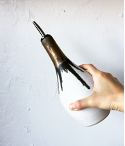 Jessica Wertz Ceramics - Gold + White Oil Bottle: Black, a handmade ceramic olive oil dispenser with a stainless-steel pour spout, held against a textured plaster wall.
