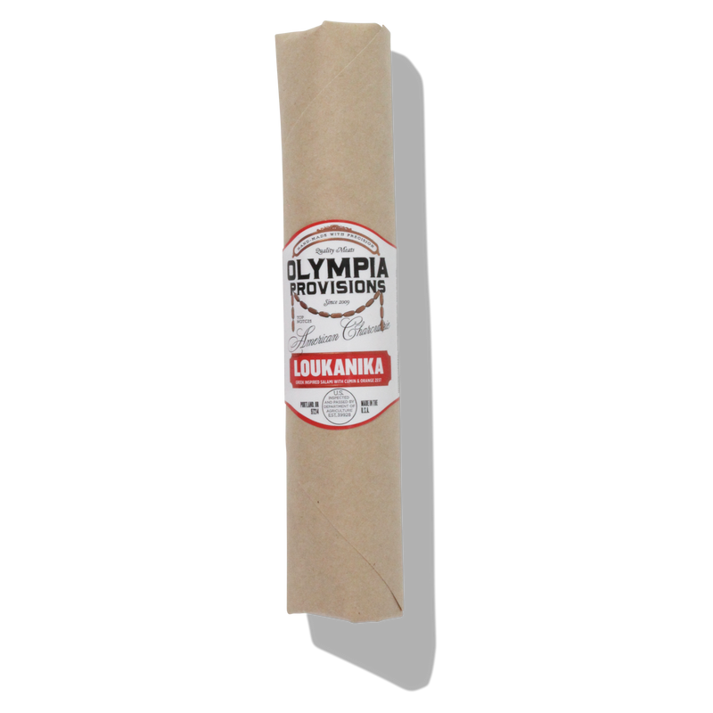 Olympia Provisions - Loukanika Salami wrapped in butcher paper; a Greek-inspired salami with cumin, garlic, and orange zest, showcasing natural mold on its casing.