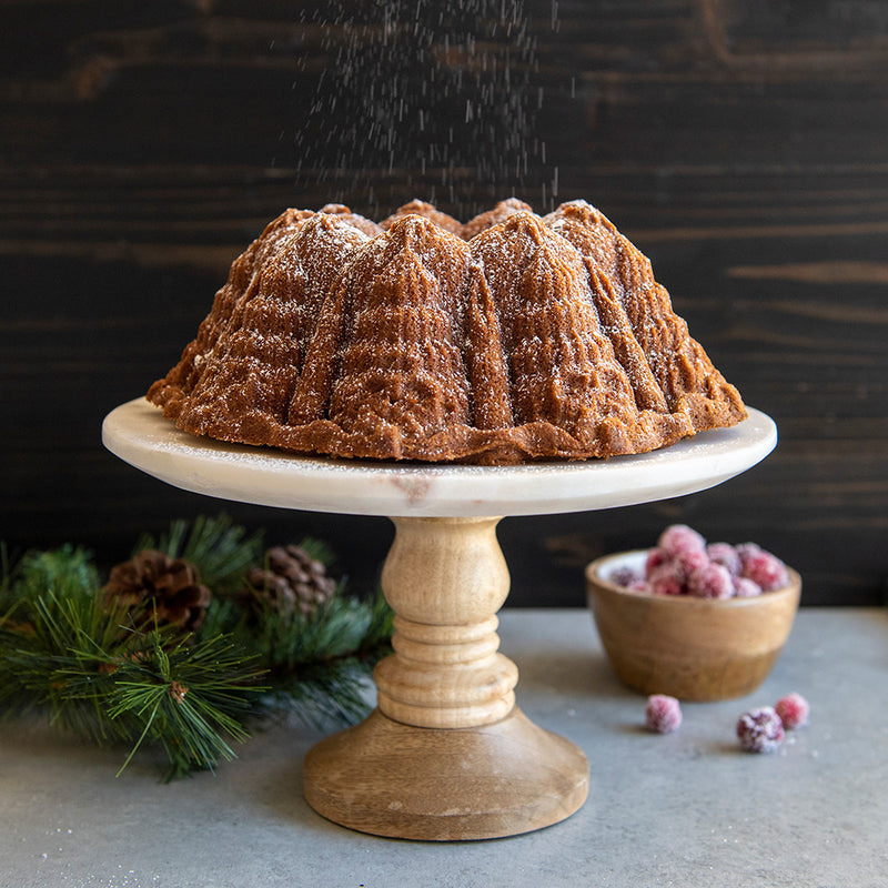 Nordic Ware | Very Merry Bundt® Pan showcasing a powdered sugar-topped cake on a stand, with intricate holiday-themed designs, ideal for festive baking.