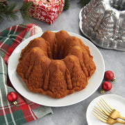 Nordic Ware | Very Merry Bundt® Pan showcasing intricate holiday designs, placed on a table with gold forks and festive decor, ideal for stunning holiday desserts.