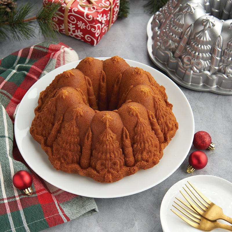 Nordic Ware | Very Merry Bundt® Pan showcasing intricate holiday designs, placed on a table with gold forks and festive decor, ideal for stunning holiday desserts.
