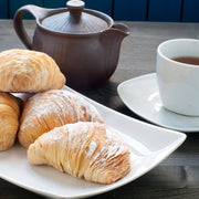 Individual Mini Italian Sfogliatelle Pastries on a white plate, paired with a teapot and cup, showcasing delicate, multi-layered treats filled with ricotta and orange peel.