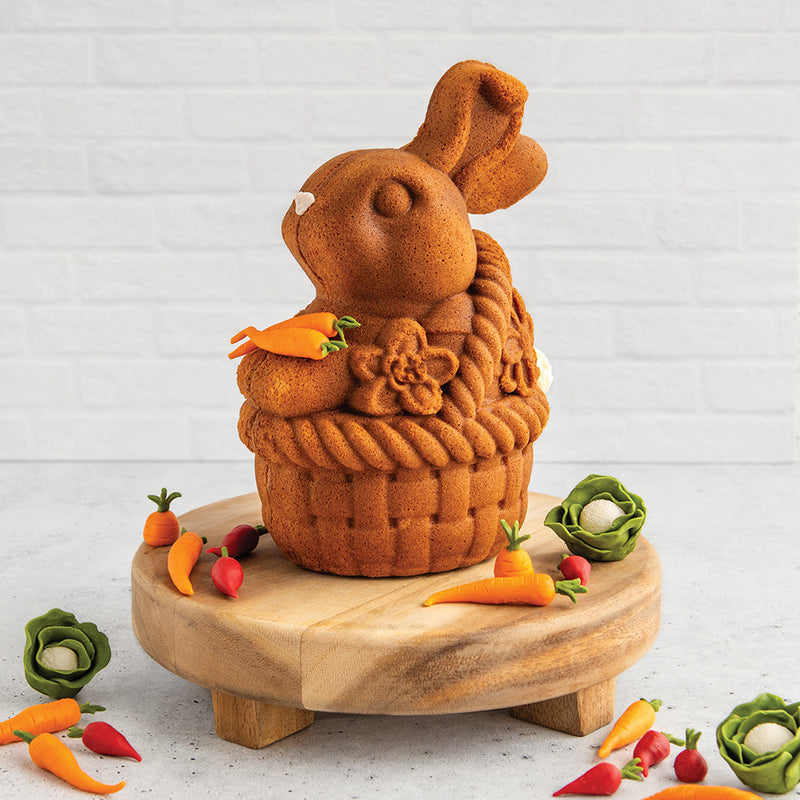 Nordic Ware Bunny In Basket 3D Cake Pan displayed with a bunny-shaped cake on a wooden board, emphasizing its intricate baking and decorating potential for Easter.