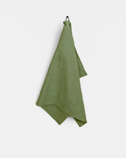Green linen tea towel with hanging loop, made from European flax, displayed on a hook. Durable and absorbent, ideal for kitchen use.