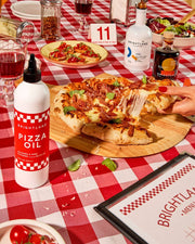 Brightland Pizza Oil enhances a Neapolitan pizza spread with bruschetta, salad, and wine, capturing the vibrant essence of a classic pizzeria setting.