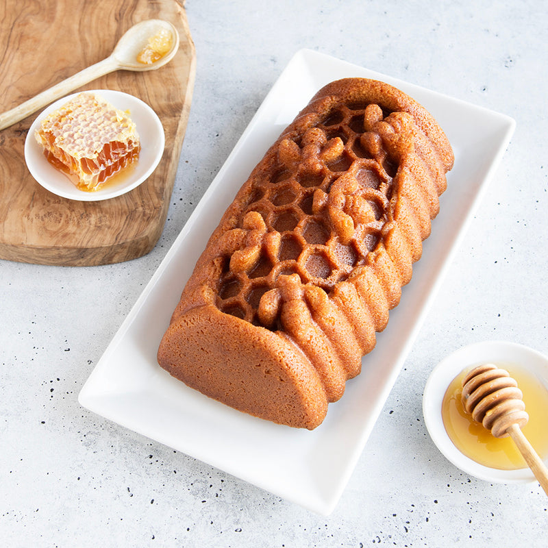 Nordic Ware | Honey Hive Loaf Pan showcasing a honeycomb-shaped loaf on a plate, accompanied by honey, highlighting the pan's unique and intricate design.