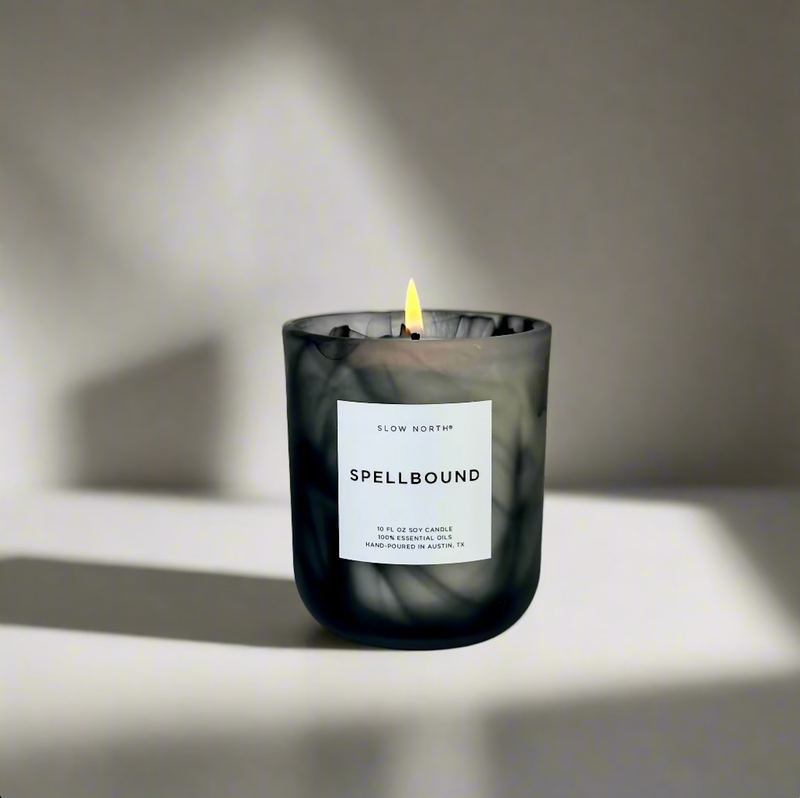 Slow North - Spellbound - Limited Edition Halloween Candle in smoky-marble glass, lit, with a label detailing essential oils, hand-poured in Austin, TX.