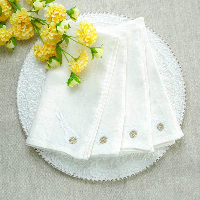 Cotton Tail Bunny Washed Linen Napkin Set featuring embroidered bunnies on white linen, arranged on a plate with yellow flowers. Perfect for Easter dining elegance.