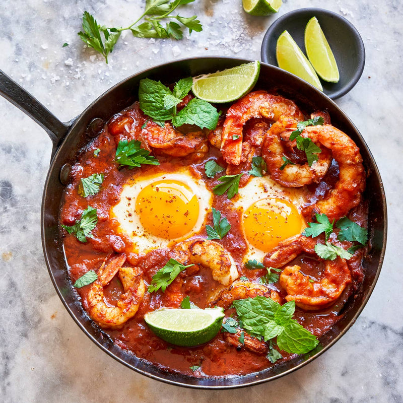 Villa Jerada - Shakshuka Blend - 50g: Skillet with shrimp shakshuka, featuring sunny-side-up eggs in tomato-pepper stew, topped with herbs, lime wedges, and coarse salt.