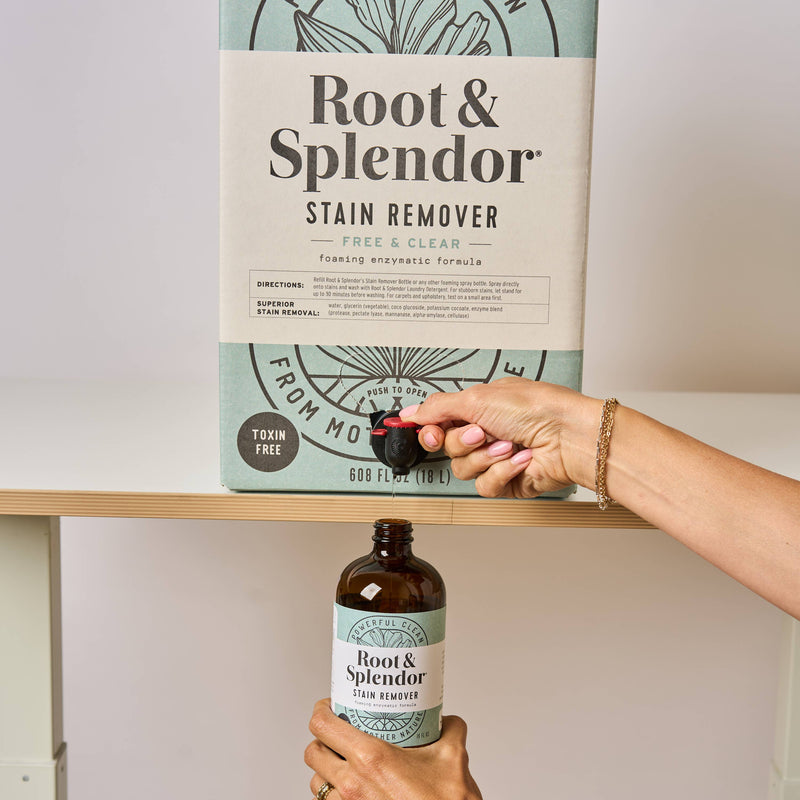 Root and Splendor - Bulk Stain Remover: 18 L box with spigot, pouring solution into amber refill bottle, ideal for eco-friendly laundry at Athens Cooks.