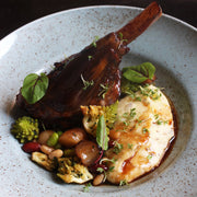Braised lamb shank with creamy mashed potatoes and vegetables, drizzled with Giusti Quarto Centenario Balsamic Vinegar, highlighted by microgreens garnish.