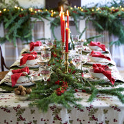 Couleur Nature - Gooseberry Red & Green tablecloth elegantly adorns a festive dining table, featuring holly patterns and a lush garland with red candles.