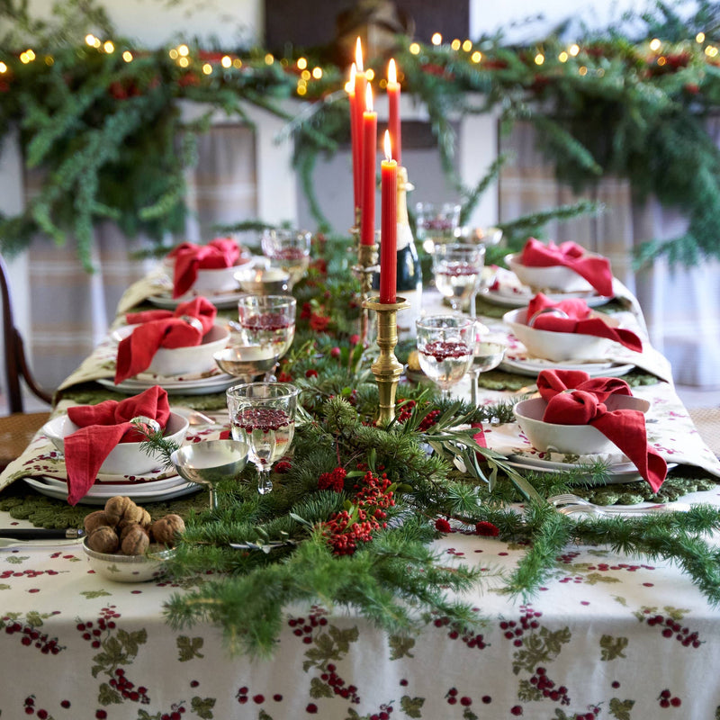 Couleur Nature - Gooseberry Red & Green tablecloth elegantly adorns a festive dining table, featuring holly patterns and a lush garland with red candles.
